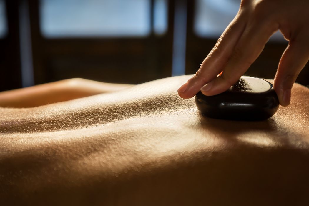 Aesthetician Placing Hot Stones Along A Client’s Back During A Relaxing Hot Stone Massage, A Popular Service Add-On At Namaste Skincare &Amp; Wellness.