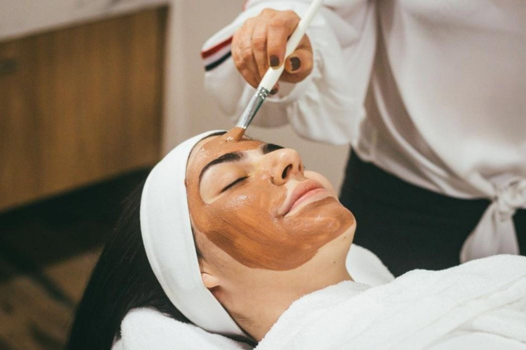 A skincare specialist at Namaste Skincare & Wellness in Henderson, Nevada performs a facial treatment as part of their spa service add-ons. The client is wrapped in white towels, creating a calm and professional spa atmosphere.