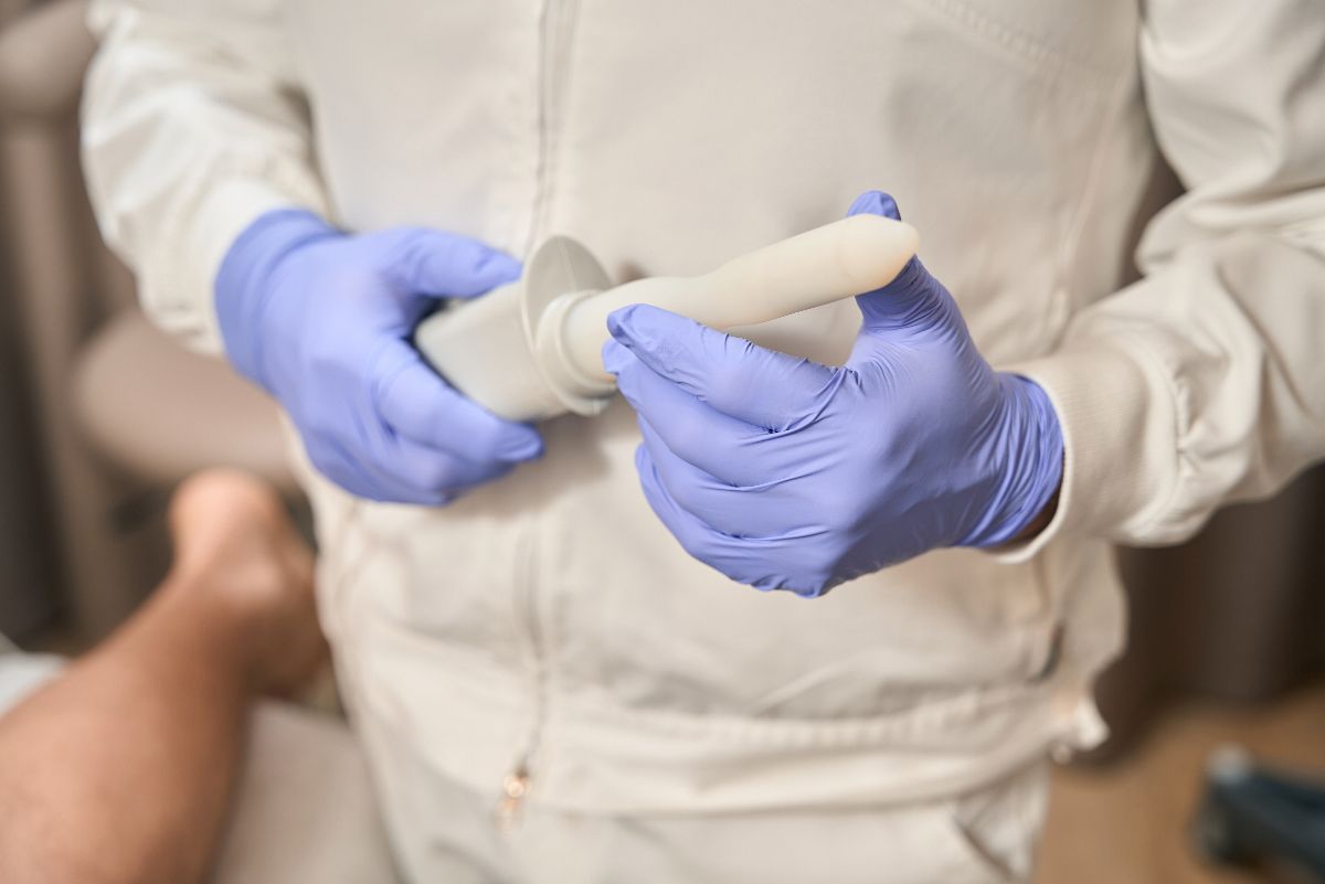A person wearing purple gloves and a white coat holds a medical device, in a clinical setting